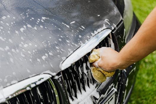 Spring Car Care: Revitalize Your Vehicle After a Long Winter Detailed view of a hand washing a car grille with a soapy sponge outdoors.